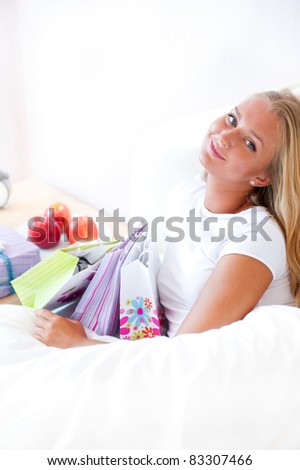 Young happy attractive girl unpack shopping bags in bedroom or hotel after enjoying being in mall. Vertical Shot