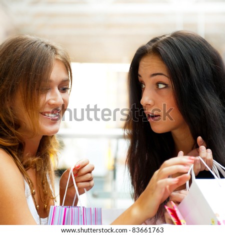 Two excited shopping woman gossip together inside shopping mall. Horizontal Shot