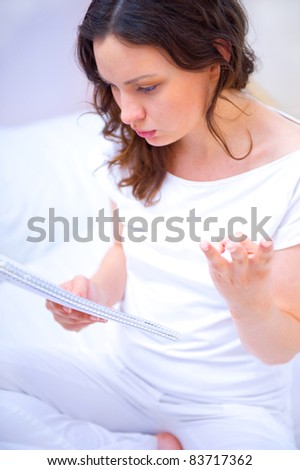 Young woman with a notebook studying at home sitting on bed. She is concentrating
