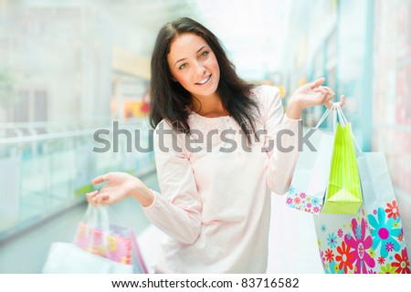 Photo of young joyful woman with shopping bags on the background of shop windows at mall. She is smiling and walking