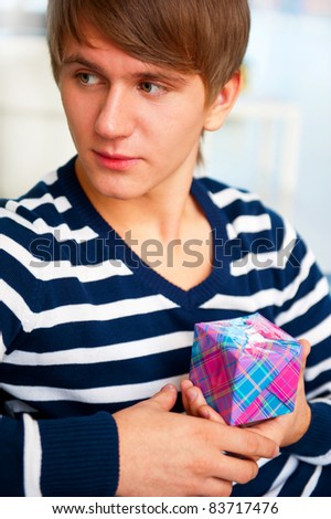 Portrait of young man inside shopping mall sitting relaxed on couch, holding box and preparing to make his couple a gift.
