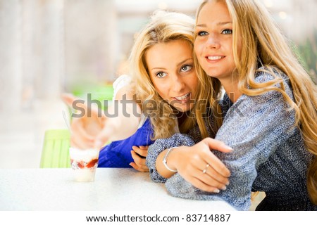 Two beautiful women drinking coffee and chatting at mall cafe. One of them pointing to copyspace and they both looking there.