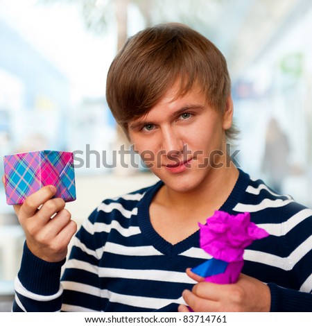 Portrait of young man inside shopping mall standing relaxed and holding gift box and bottle. He is preparing to visit his girlfriend and make a proposal