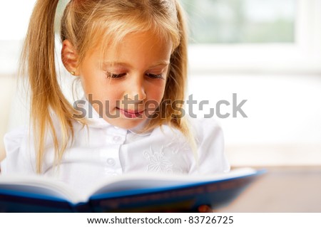 Image of smart child reading interesting book in classroom. Horizontal Shot. She is involved and thinking
