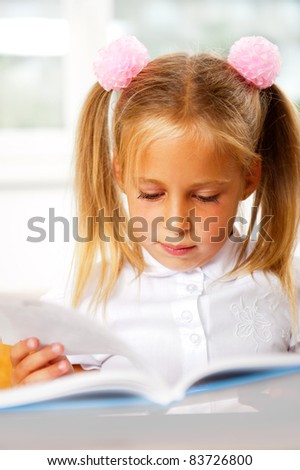 Image of smart child reading interesting book in classroom. Vertical Shot. She is involved and attentive