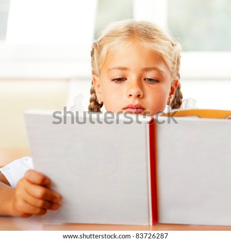 Image of smart child reading interesting book in classroom. Horizontal Shot. She is involved and thinking