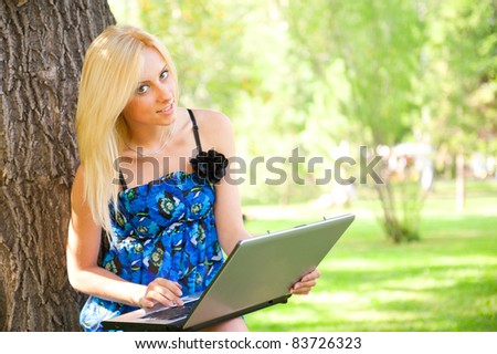 Portrait of a pretty student woman leaning on the tree trunk on foreground at summer park