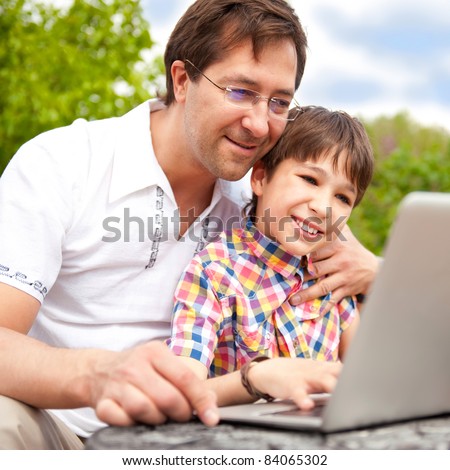 Closeup portrait of happy family: father and his son using laptop outdoor at their backyard sitting on the bench
