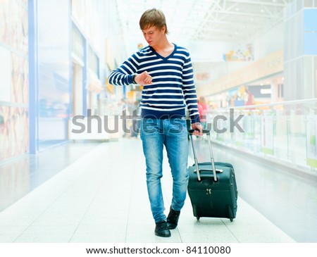 Portrait of young man walking inside modern airport with trolley bag wearing stylish casual clothes