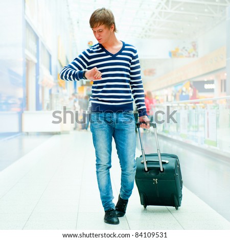 Stylish man with suitcase and passport walking along airport