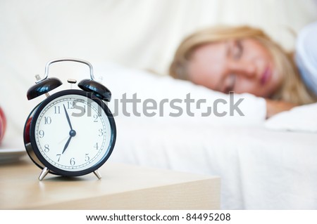 Woman sleeping in bed and alarm-clock (focus on alarm clock)