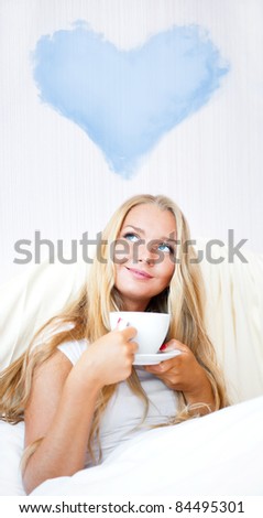 Young woman at home sipping tea or coffee from a cup and thinking about her couple. Blank balloon cloud in heart shape overhead