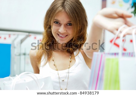 Photo of young joyful woman with shopping bags on the background of shop windows inside shopping mall