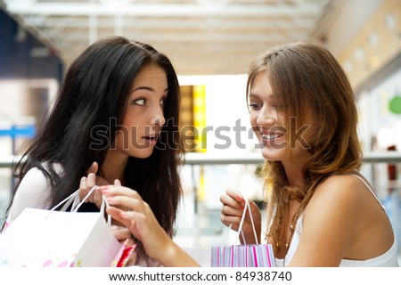 Two excited shopping woman gossip together inside shopping mall. Horizontal Shot