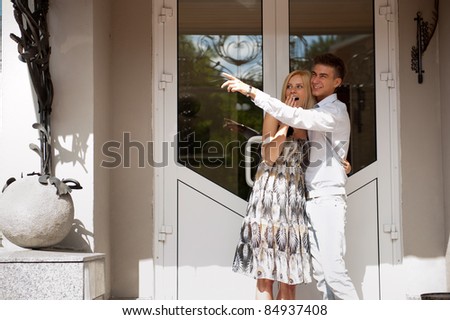 Young man embracing smiling girlfriend near door into new house, man pointing away