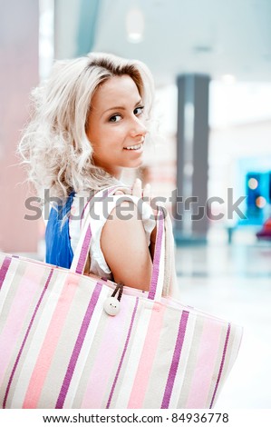 Photo of young joyful woman with shopping bags on the background of shop windows inside big mall