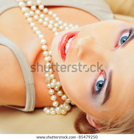 Portrait of gorgeous relaxed young lady with beautiful blue eyes smiling while lying on comfortable sofa - indoors, looking at camera