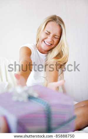 Boyfriend making a gift to his girlfriend in the morning. She is sitting on bed and taking gift box. Smiling laughing and very happy