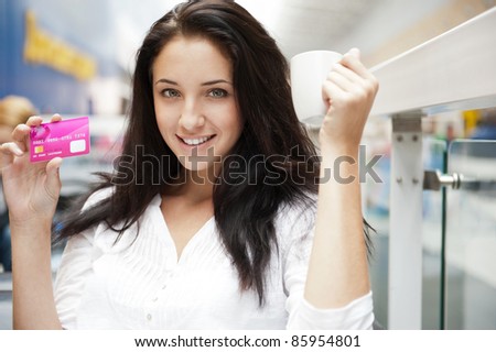 Closeup portrait of a pretty young female having a cup of coffee and holding credit card while resting at shopping mall or tax free zone of airport
