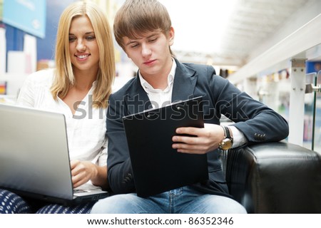 Two students working on their college project at hall using laptop and papers