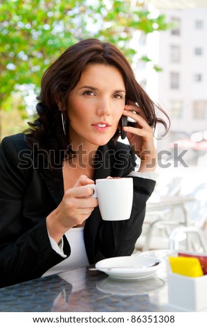Portrait of young business woman sitting relaxed at outdoor cafe drinking coffee and chatting using her cell phone