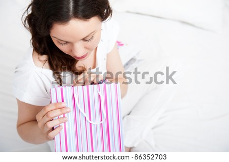 Portrait of young beautiful awake woman with gifts on bed at bedroom
