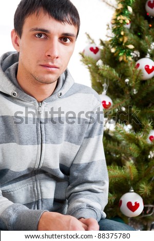 Young calm man sitting in front of Christmas tree