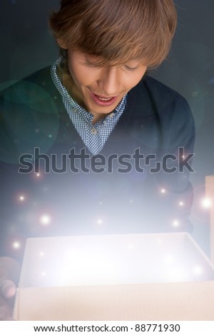 Portrait of young man opening gift box. He is happy. Magical shine inside box