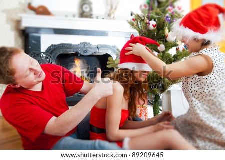 Young happy family near a Christmas tree at home holding gift and warming from fireplace