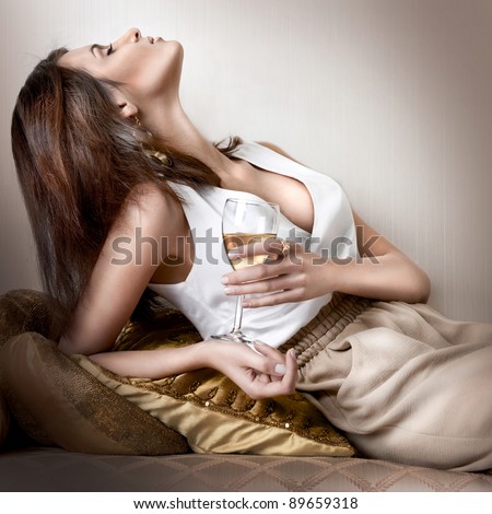 Closeup fashion portrait of young sexy hot woman sitting relaxed on comfortable luxury sofa in vintage interior and drinking champagne or wine - stock photo