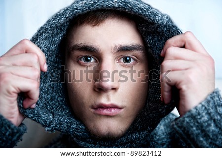 Portrait of young handsome man putting on warm pullover and looking at camera. He is hiding from the world and society. Gay discrimination concept