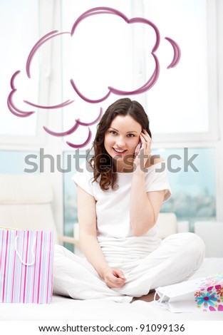 Portrait of young beautiful awake woman with gifts on bed at bedroom. Talking with her boyfriend by mobile phone. Cloud balloon overhead