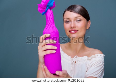 Portrait of young pretty woman holding bottle of prefect wine in gift decorative package against grey background.