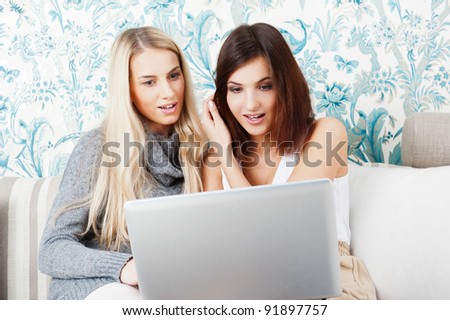 Two young women friends chatting at home and using laptop to look at new photo or browsing internet for information
