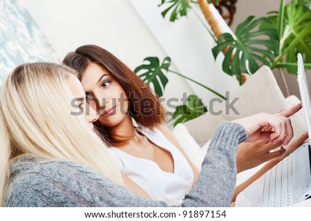 Two young women friends chatting at home and using laptop to look at new photo or browsing internet for information