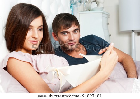 Closeup portrait of a happy young couple relaxing on the bed. Man making a gift to his girlfriend. Saint Valentine`s day concept