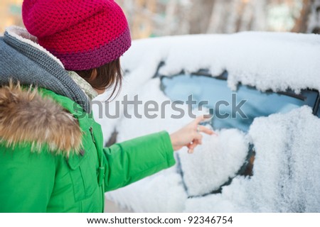 Beauty woman in the winter clothes drawing heart on car
