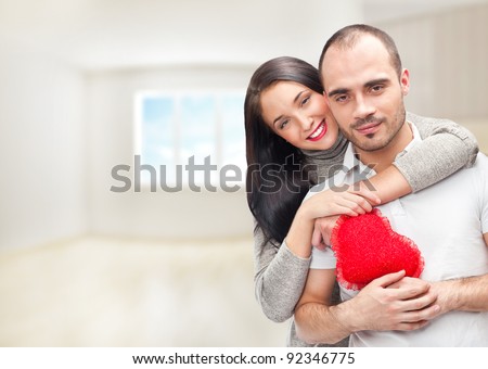 Portrait of young couple with red heart standing at their home and embracing. They are really happy to be together
