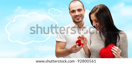 Happy young man gifting a ring to a beautiful surprised young woman on romantic background with sky and clouds with lots of copyspace