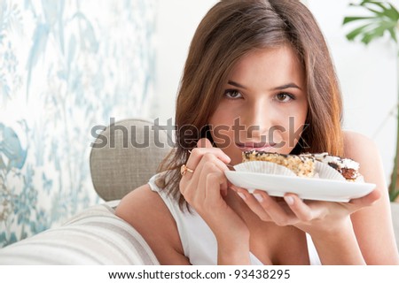 Smiling brunette woman eating some cake in the living room in her apartment