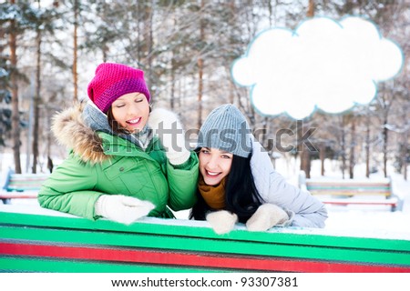 Two happy young girls having fun in winter park. Blank cloud balloon with copyspace for your text and logo