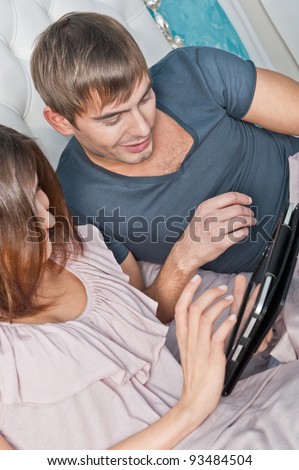 Young lively couple using tablet PC in their bed and daydreaming