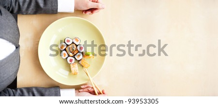 Top view of young business woman wearing suit holding sushi sticks in her arms. Sushi rolls set on plate. Business lunch offer concept