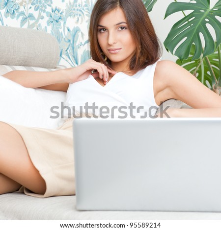 Portrait of pretty happy young woman sitting on couch with a laptop