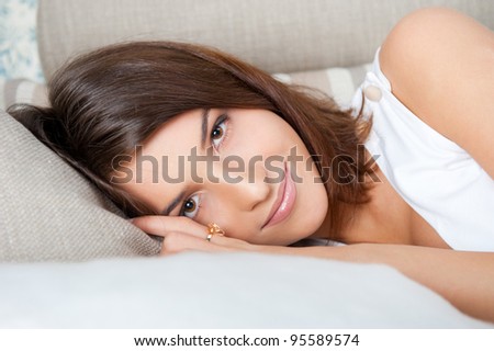 Beautiful Smiling Woman resting on sofa at home and looking at camera