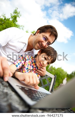Closeup portrait of happy family: father and his son using laptop outdoor at their backyard sitting on the bench