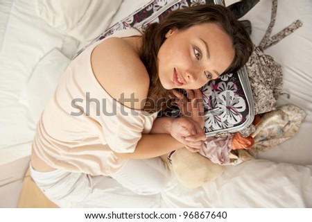 Beautiful young slim woman on the bed indoors unpacking clothes from suitcase