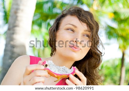 Portrait of young pretty woman wearing bright pink dress eating exotic asian dragon fruit and enjoying her vacation at tropical resort