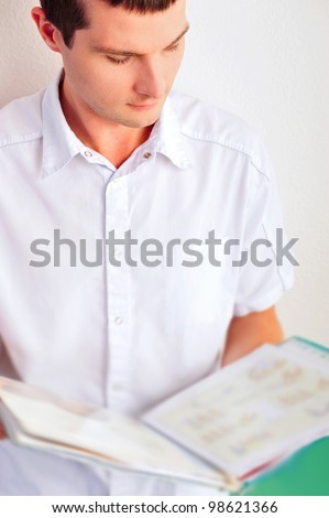 Male doctor holding reading patient`s card - leaning on the wall at hospital.