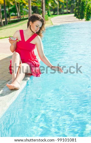 Woman sitting in a swimming pool and eating dragon fruit